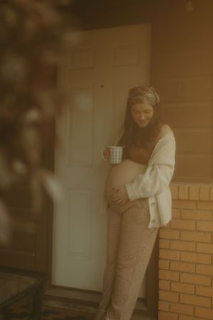 Golden-hour vintage maternity photo with soft focus showing pregnant woman holding coffee cup.
