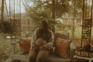 Warm-toned pregnancy photo on outdoor swing with decorative pillows.