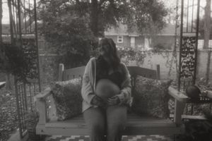 Black and white maternity portrait on porch swing shows peaceful moment.