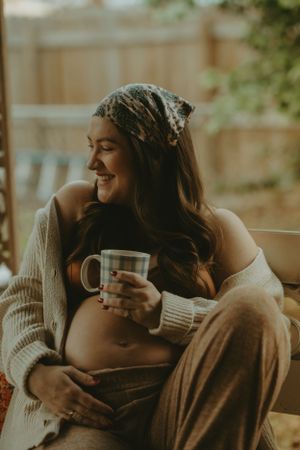 Candid maternity moment captured in warm sunlight on decorated porch swing.