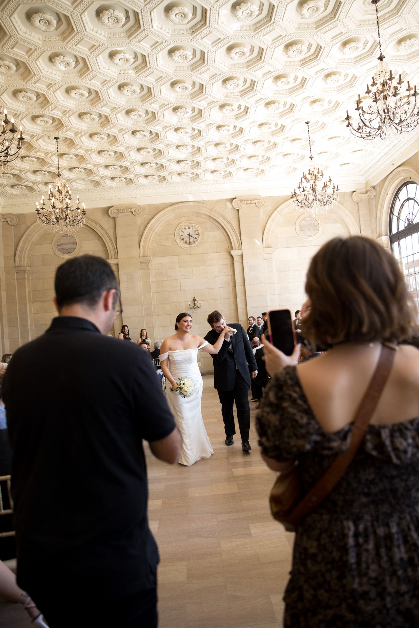 Elegant ballroom with ornate ceiling, chandeliers and guests dancing.