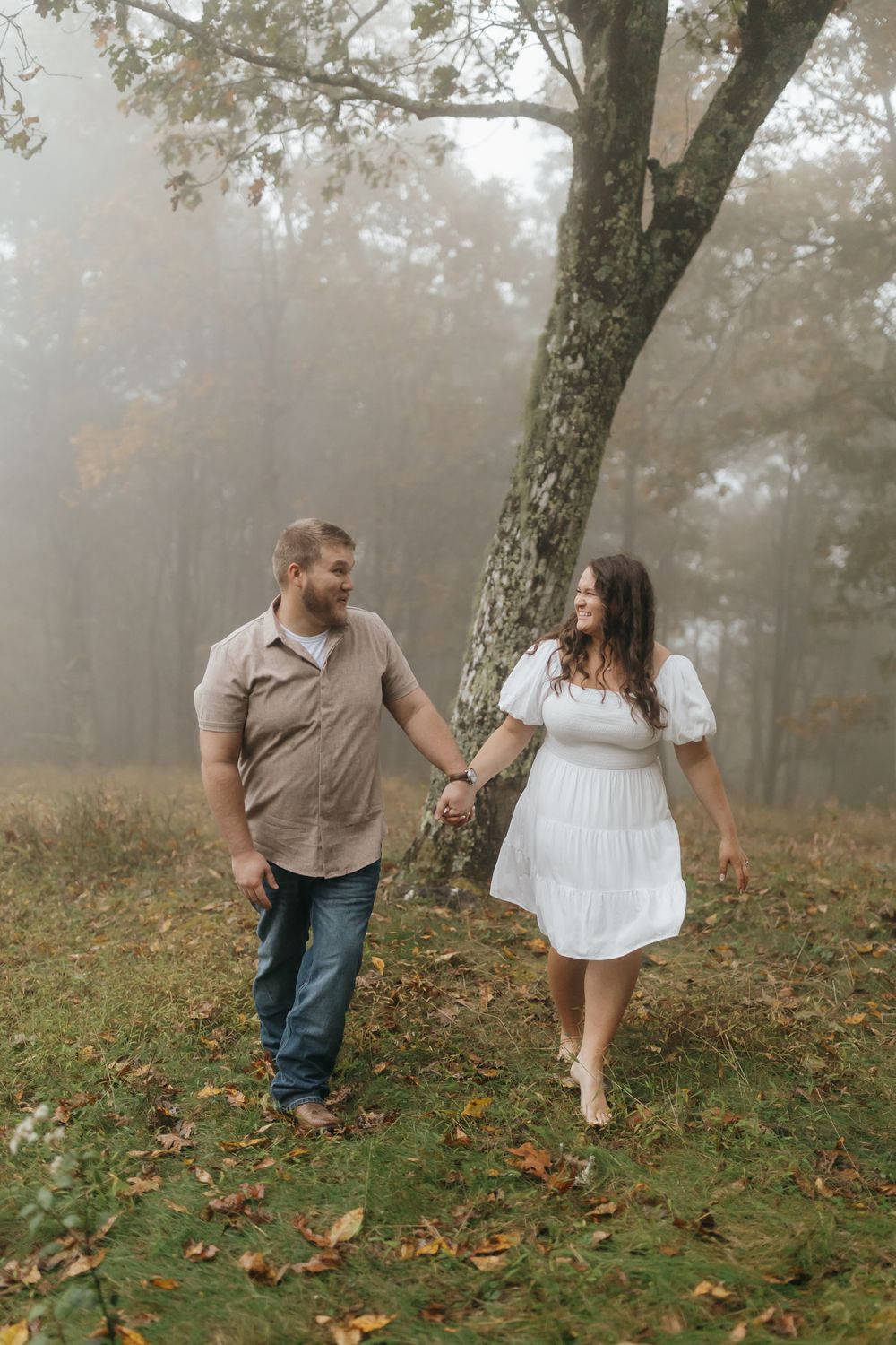 A couple takes a romantic walk through a misty forest clearing in autumn.