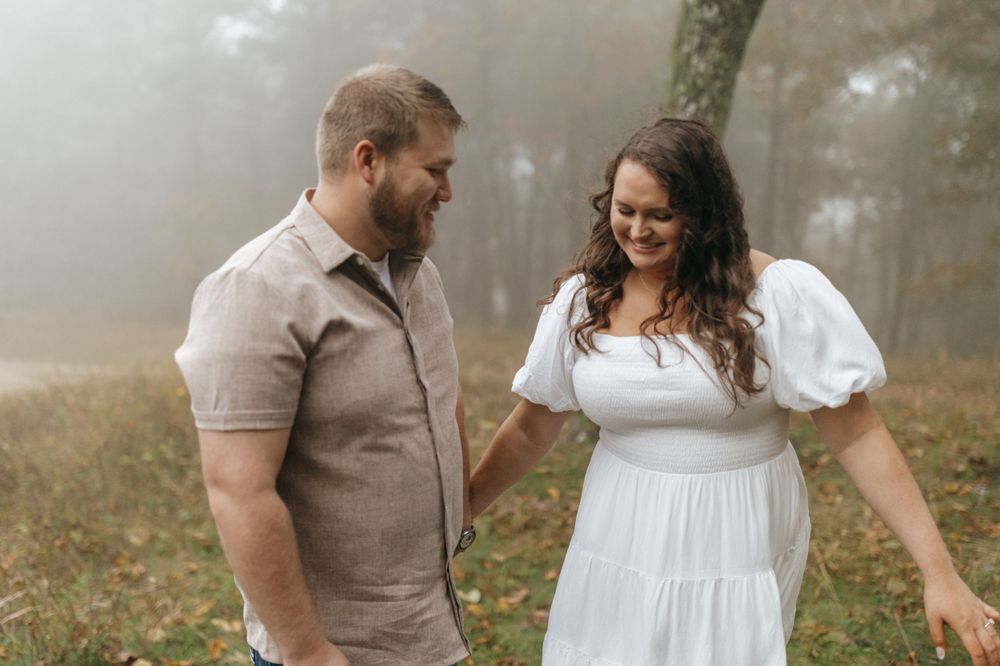 A couple shares a playful moment in a foggy autumn setting wearing coordinated casual outfits.
