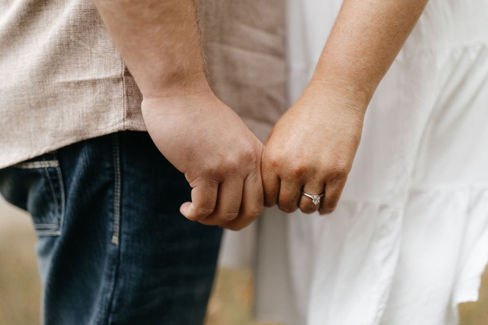 A close-up shot of two people holding hands showing interlocked fingers and a sparkly ring.