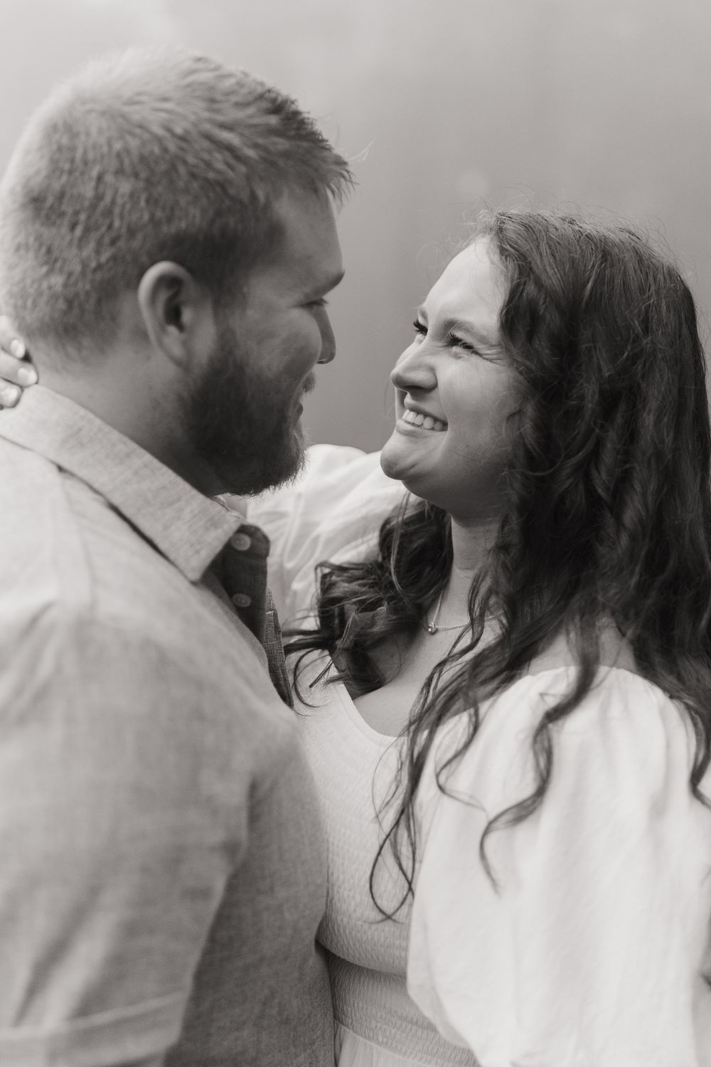 A romantic black and white portrait of a couple sharing a joyful moment on a foggy day.