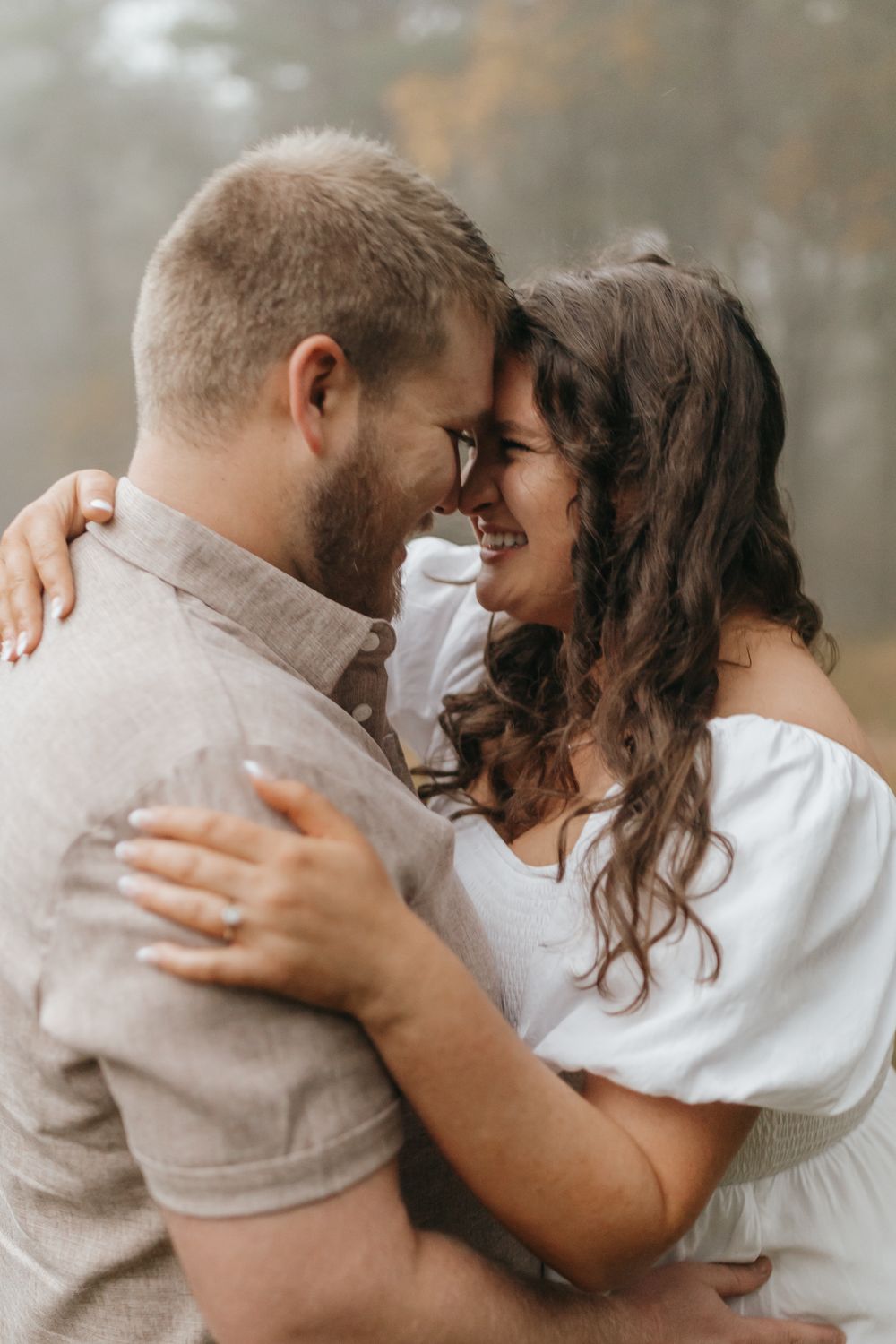 A romantic close-up of a couple embracing with foreheads touching in a misty outdoor setting.