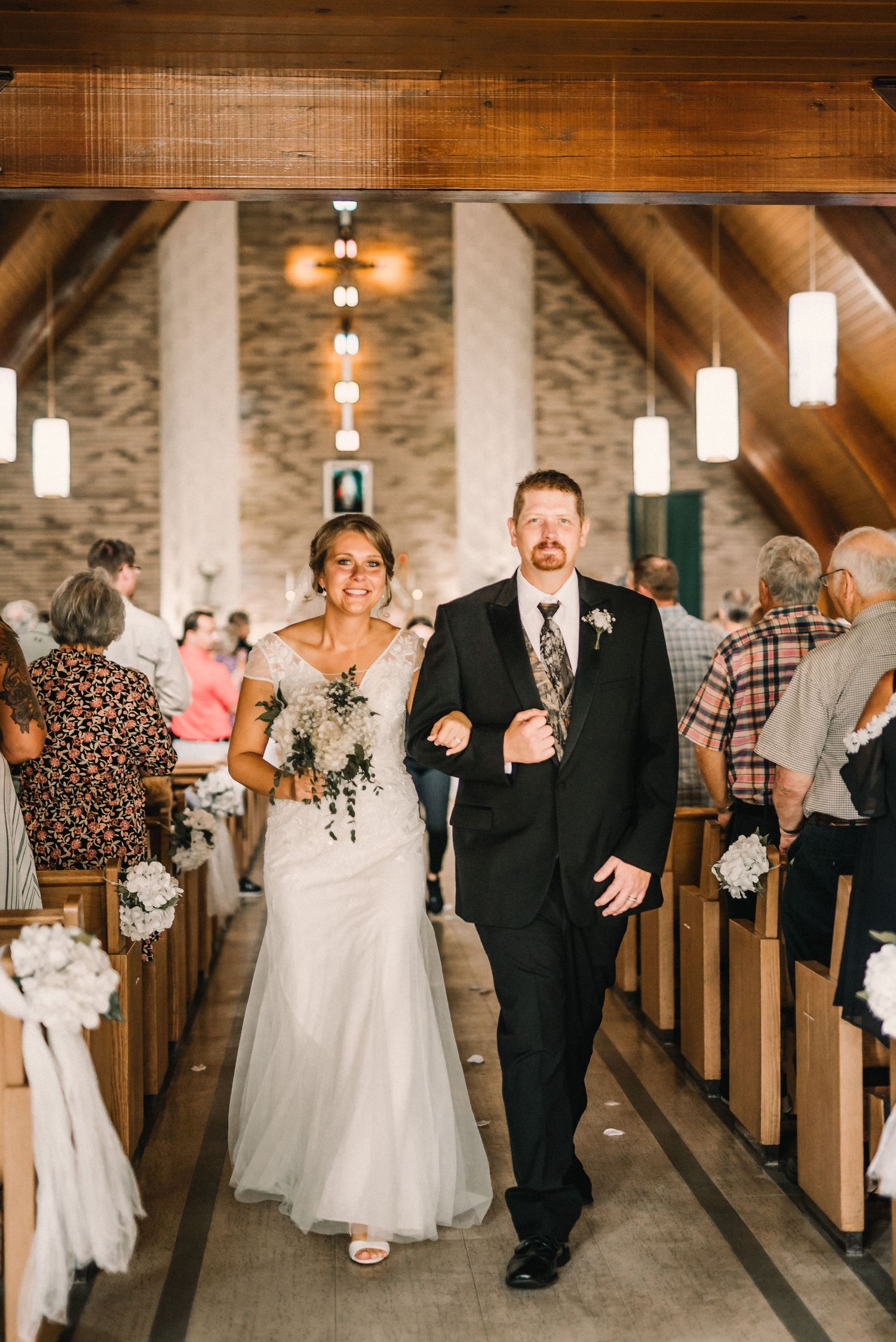 Wedding ceremony in rustic church with wooden beams and hanging lights.