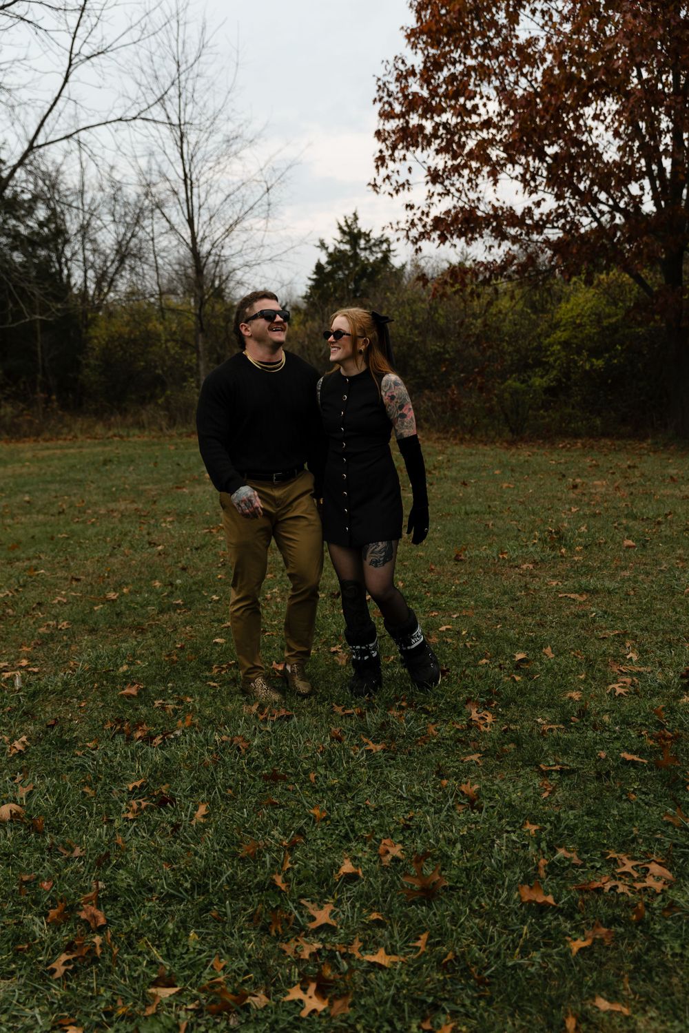 A couple walks together through fallen autumn leaves in a park setting.
