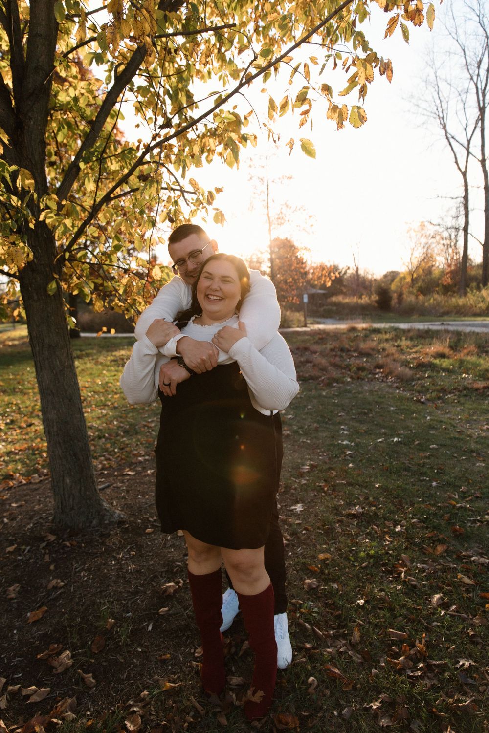 Joyful couple embracing and laughing under golden autumn leaves.