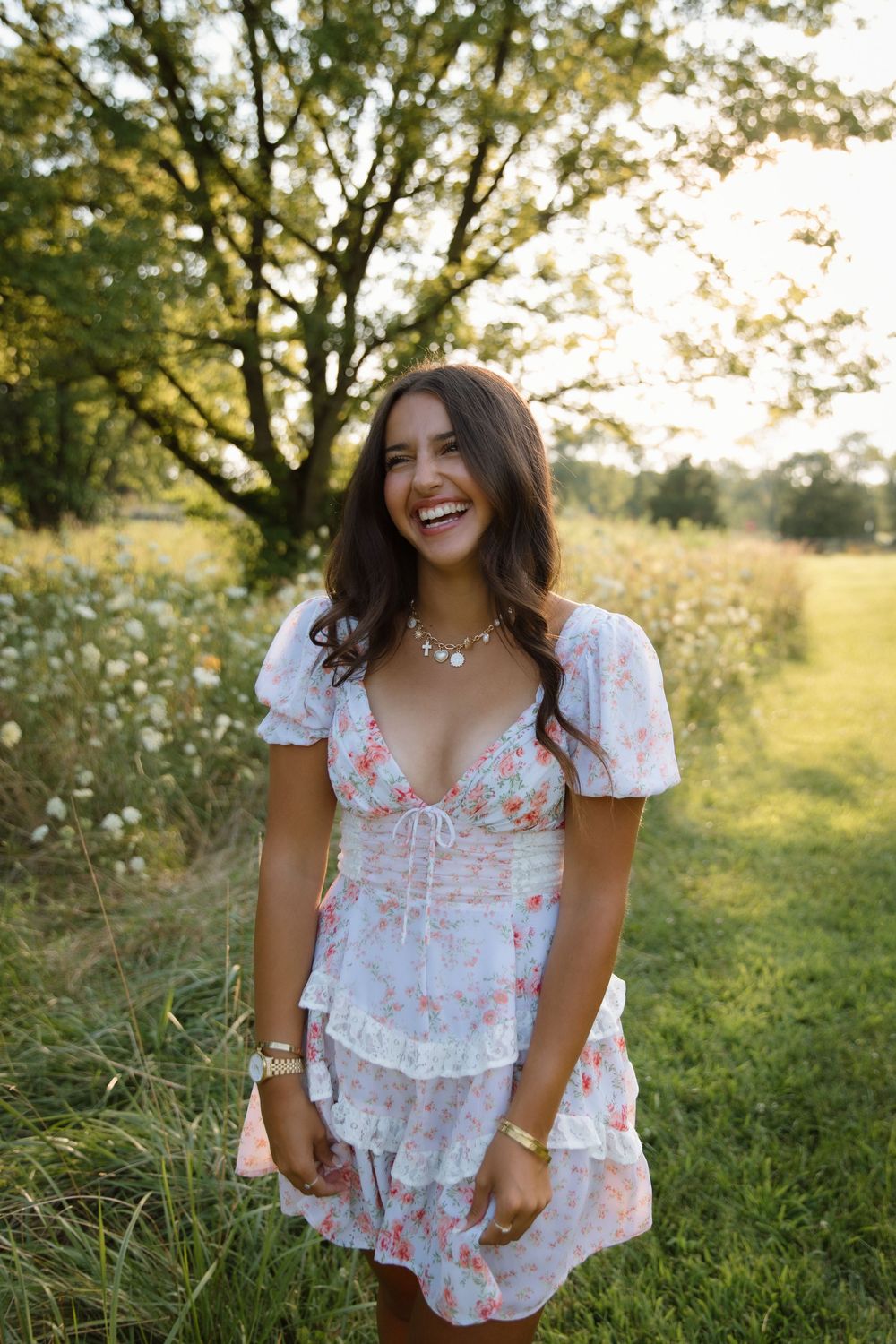 A floral white dress with puff sleeves is pictured in a sunny meadow setting at golden hour.