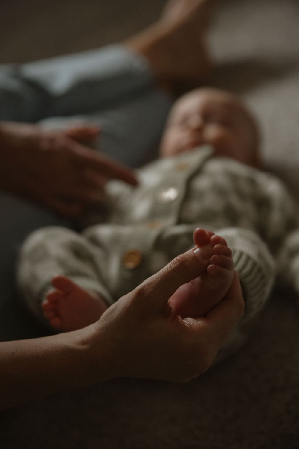 Close-up of tiny baby feet being gently held by adult hands in a dimly lit setting.
