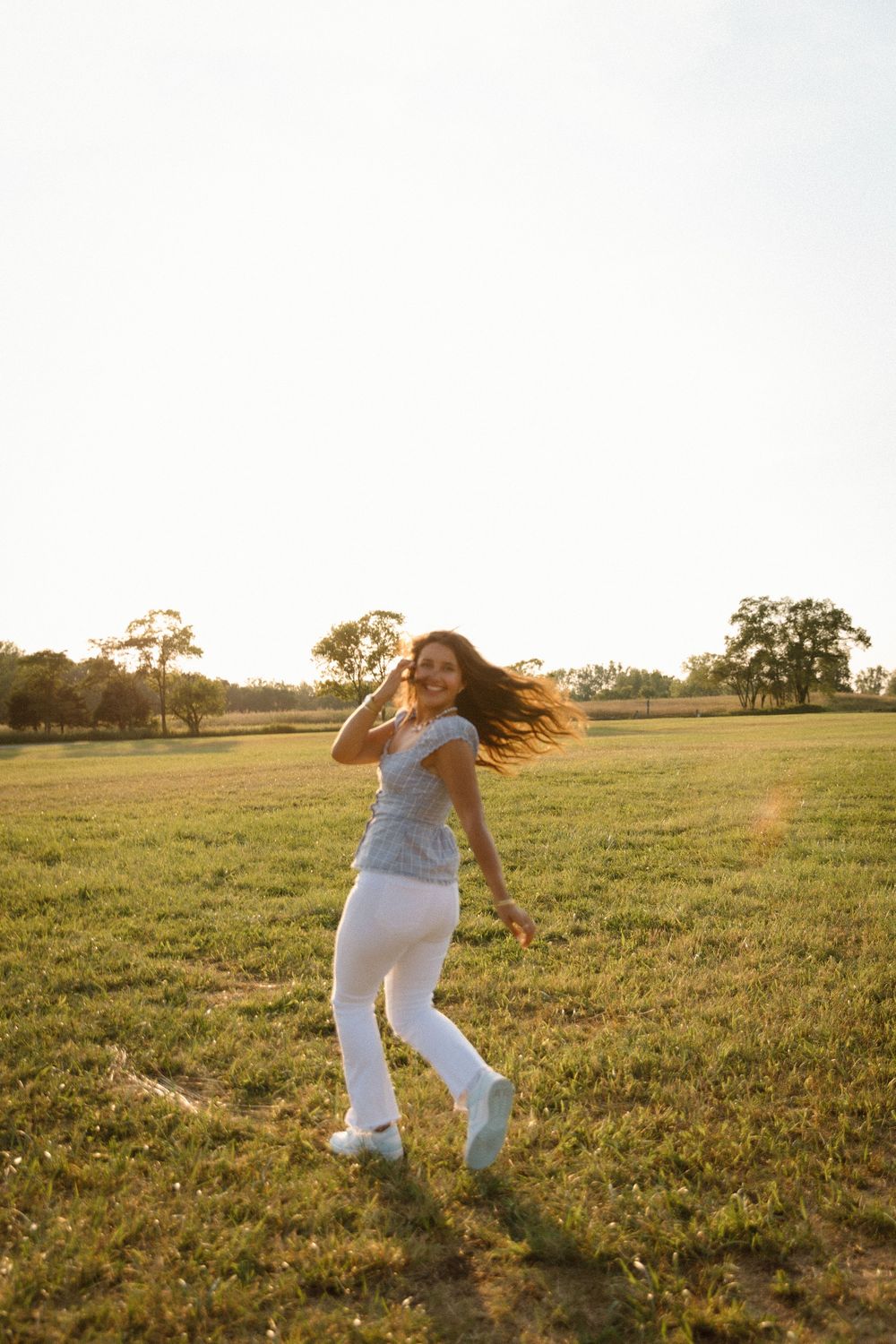 Person wearing white pants dances freely in a golden sunlit field at sunset, creating a dreamy summer moment.