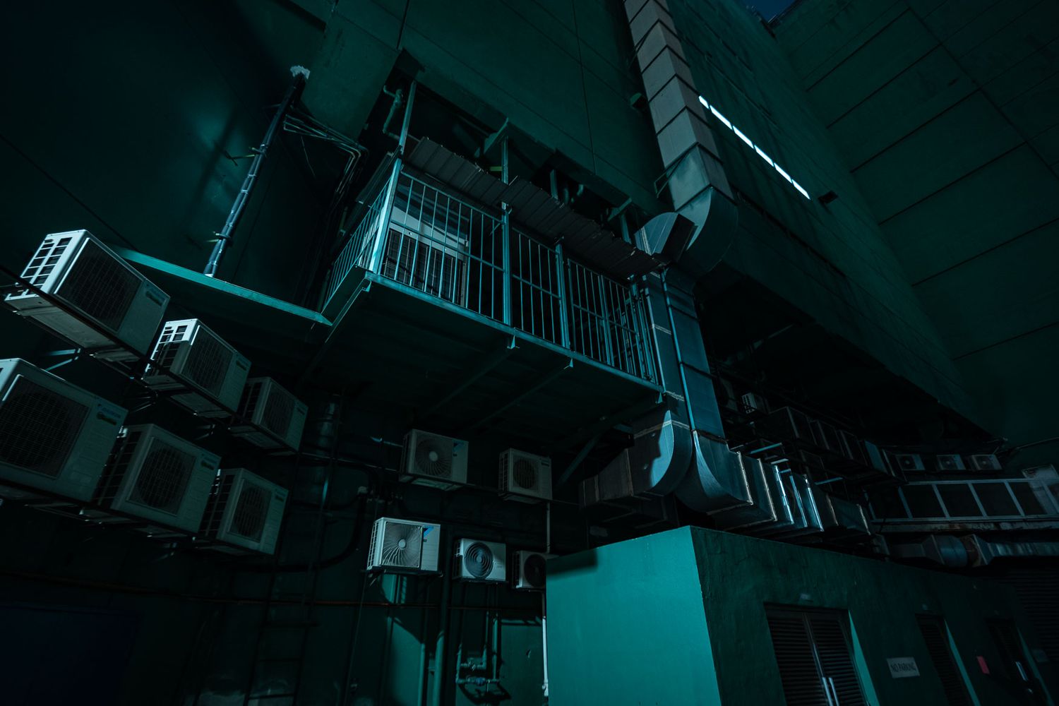 Dark and moody low-angle architectural shot of a building interior with teal lighting and geometric structural elements.