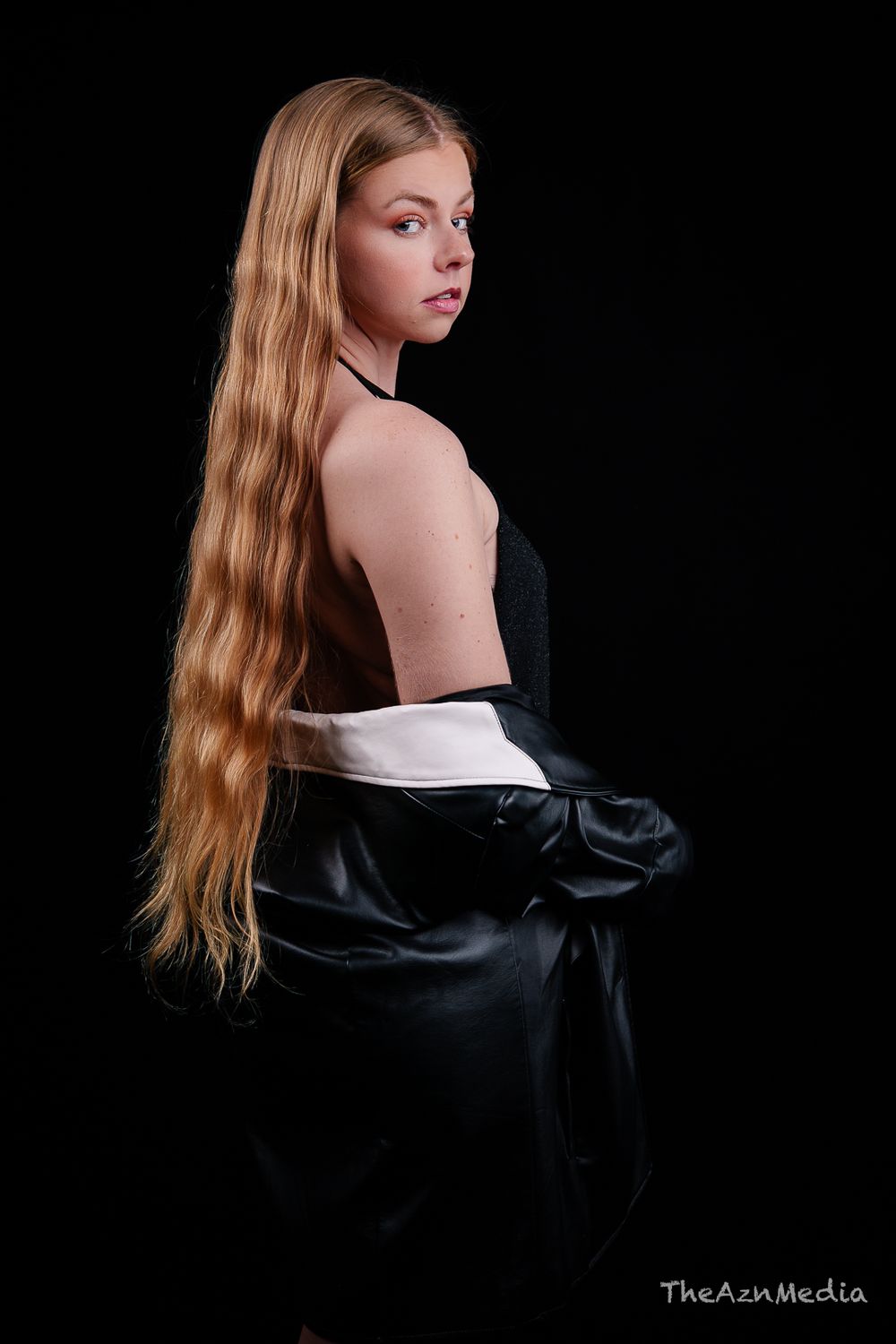 Fashion portrait showing long blonde hair and black leather jacket against dark background.