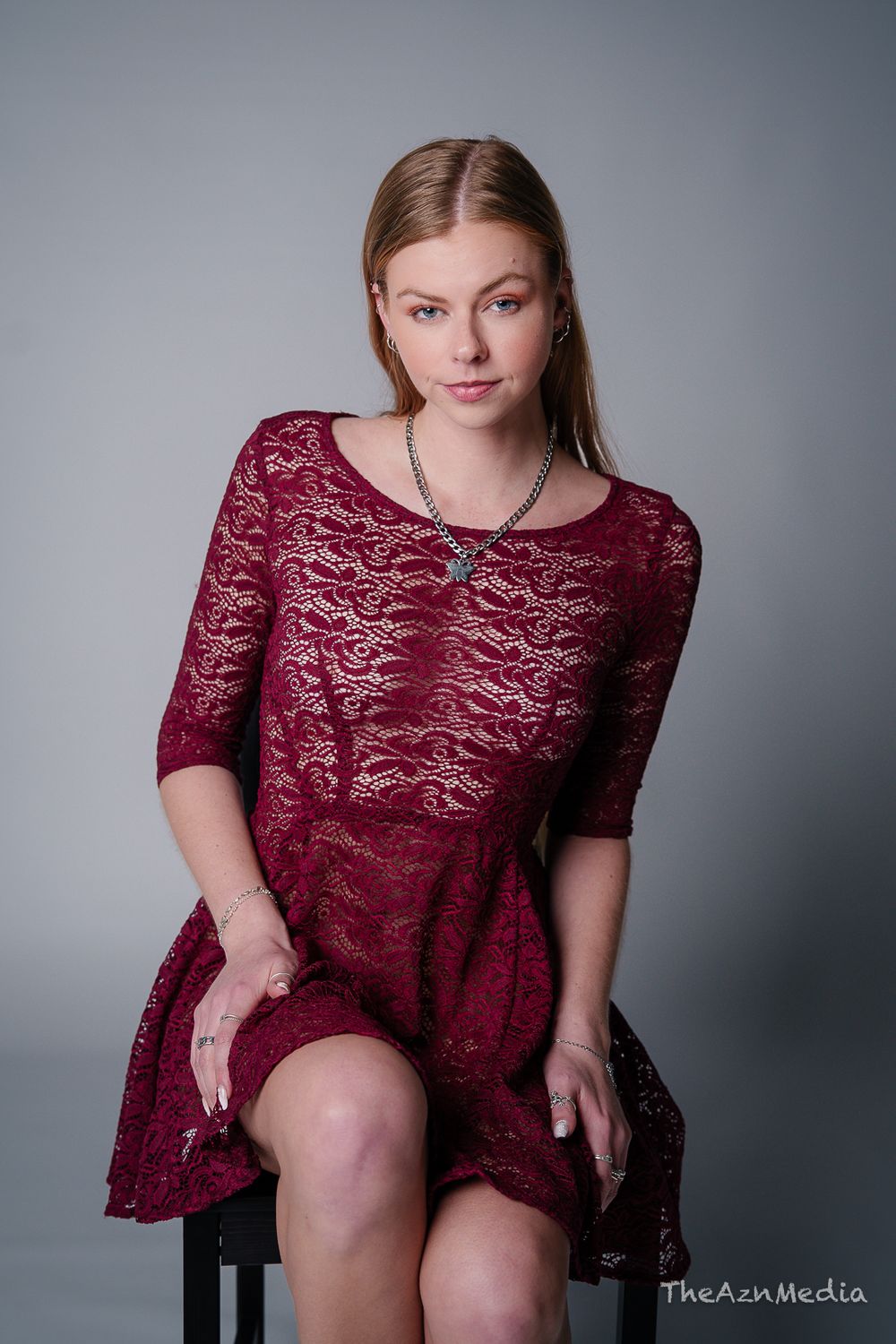 Portrait in burgundy lace dress seated against grey studio background.