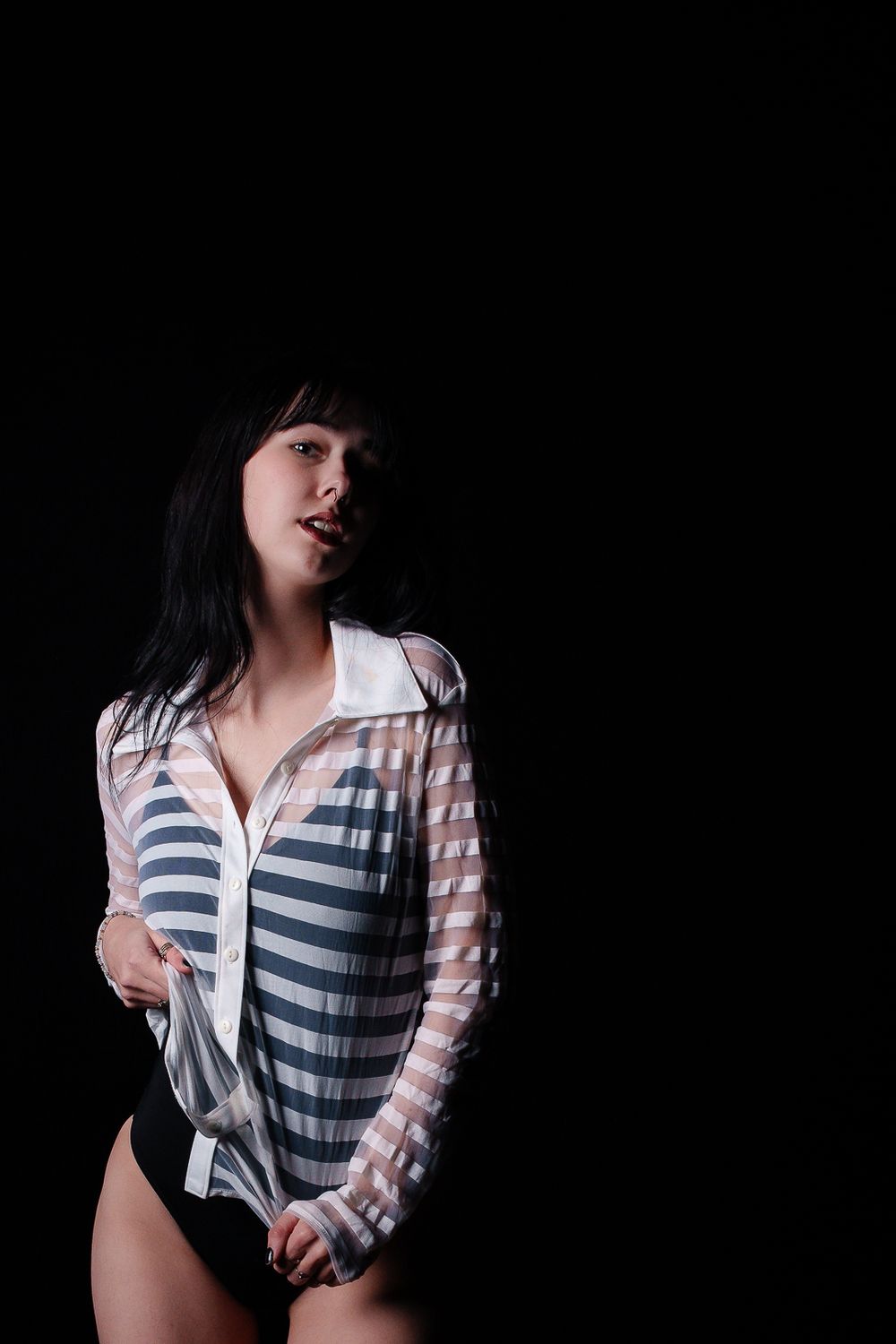 Moody portrait in striped sheer bodysuit against dark background.