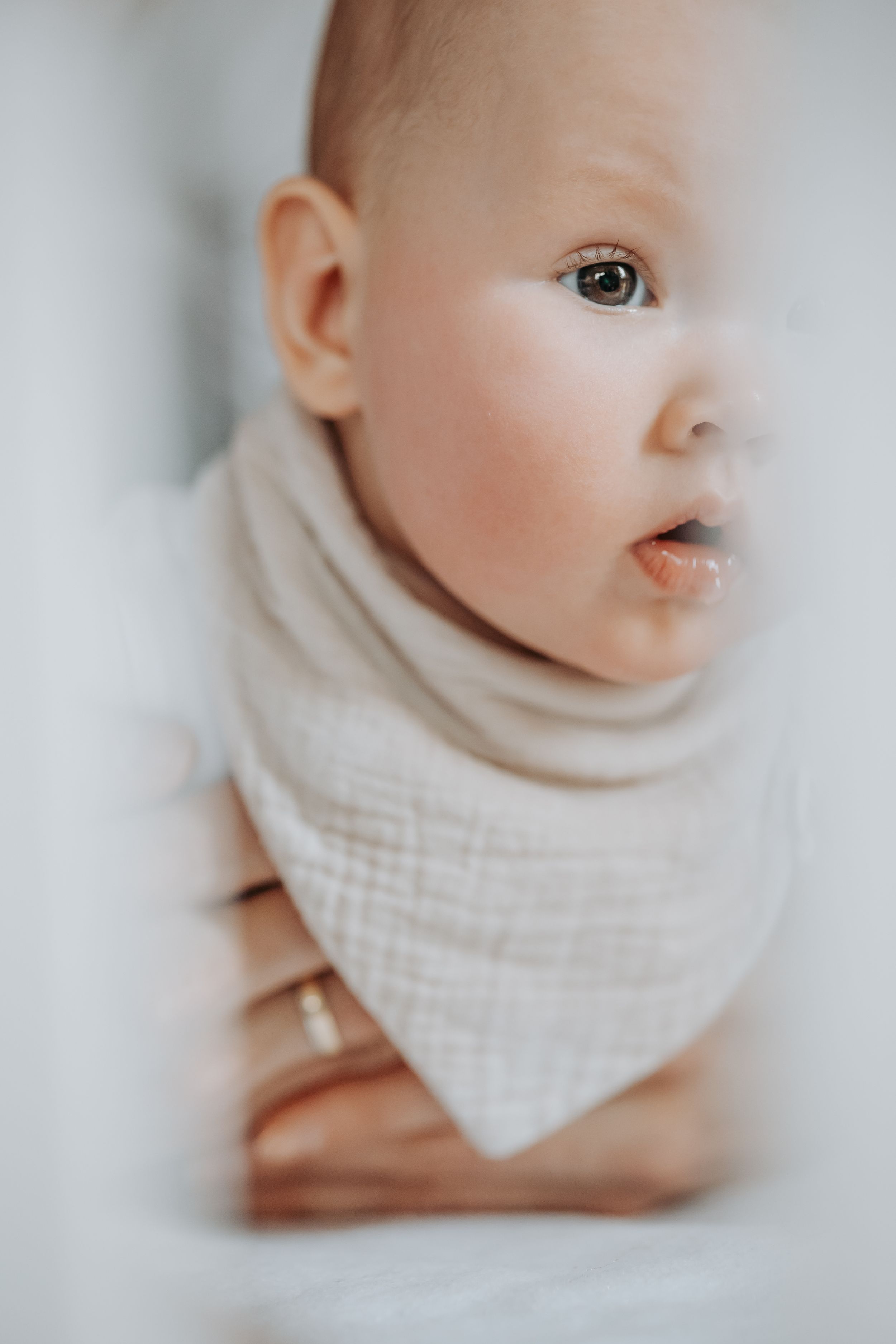 Sweet baby wearing beige cotton bandana bib photographed in dreamy soft focus with shallow depth of field.