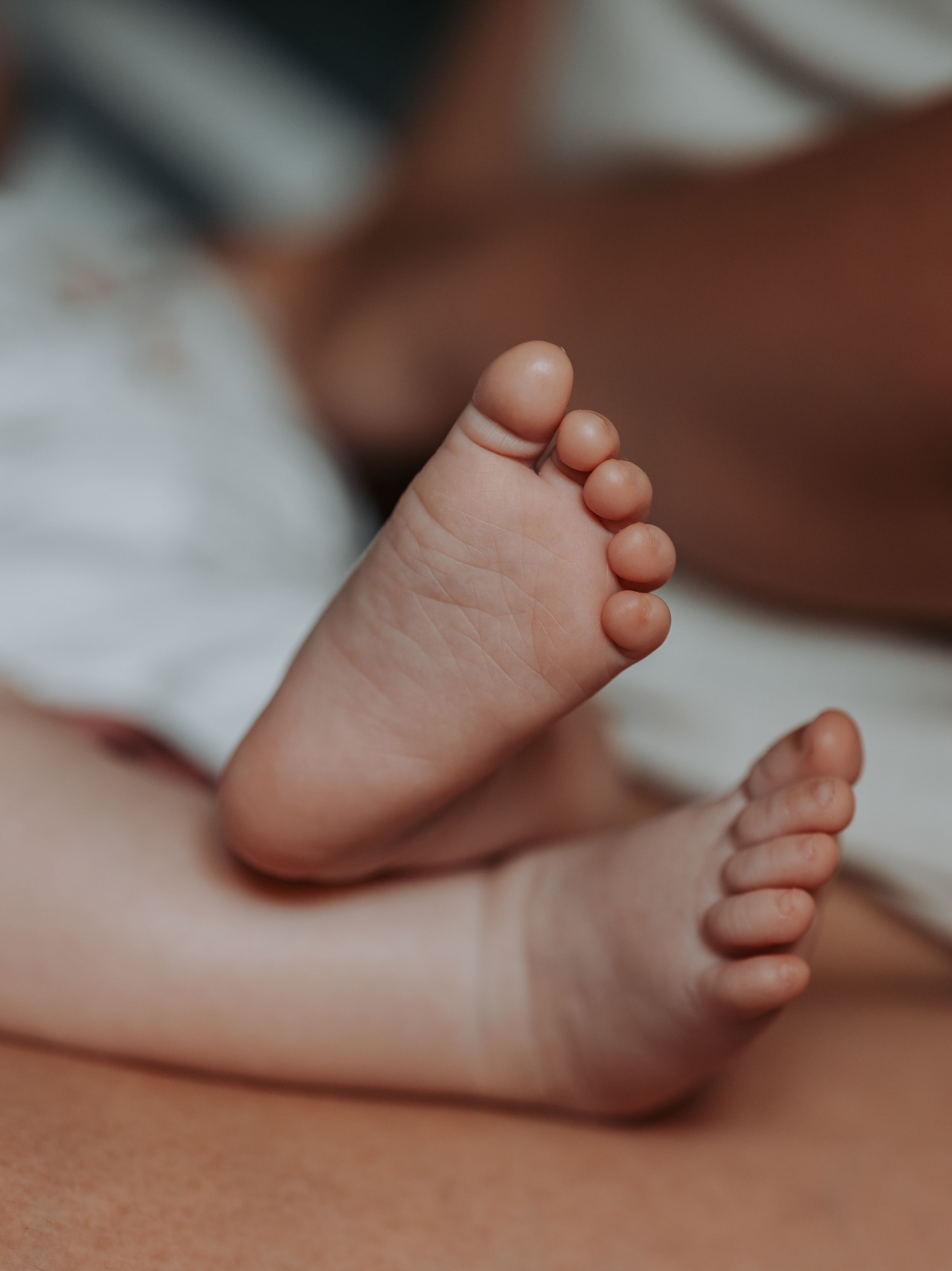 Close up of tiny baby feet resting on a soft surface in natural lighting.