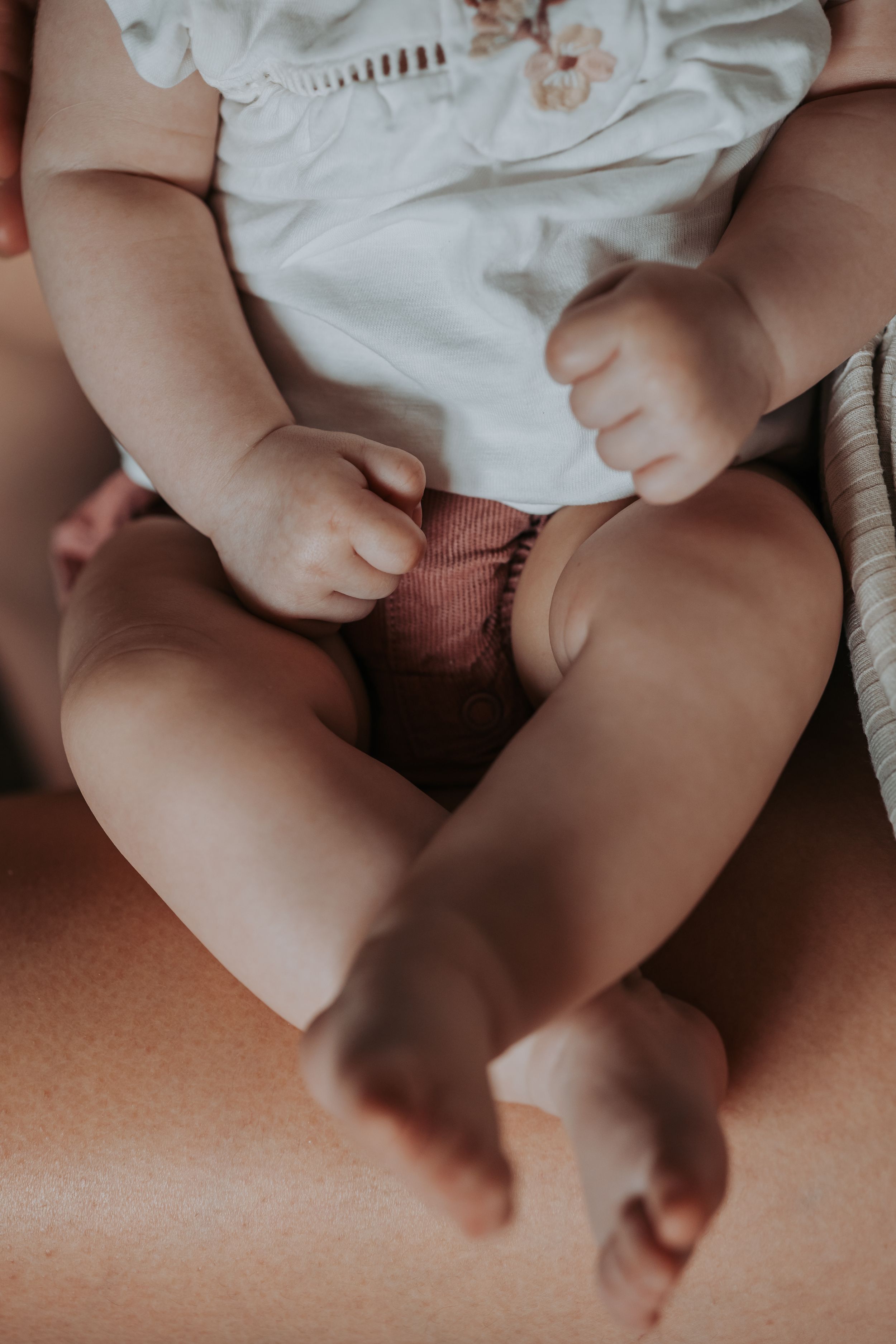 Close-up of a baby's chubby legs and feet wearing white clothing and a pink diaper while resting comfortably.