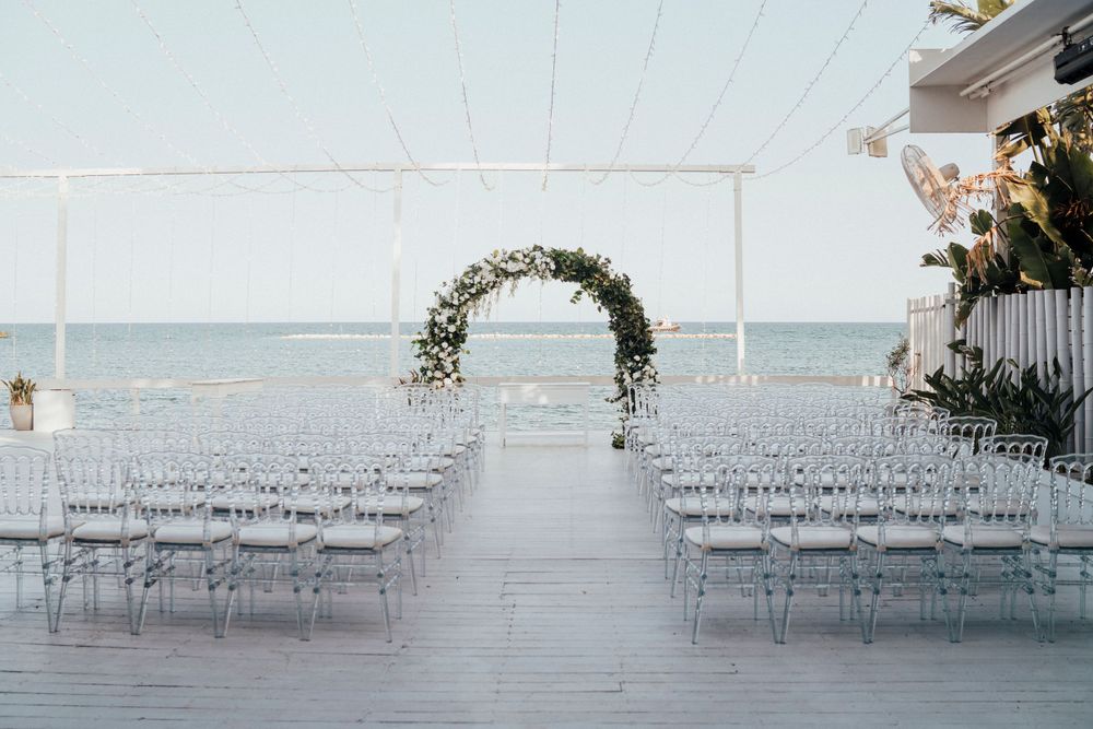 Elegant white wedding ceremony setup with floral arch overlooking the ocean under a white tent canopy.