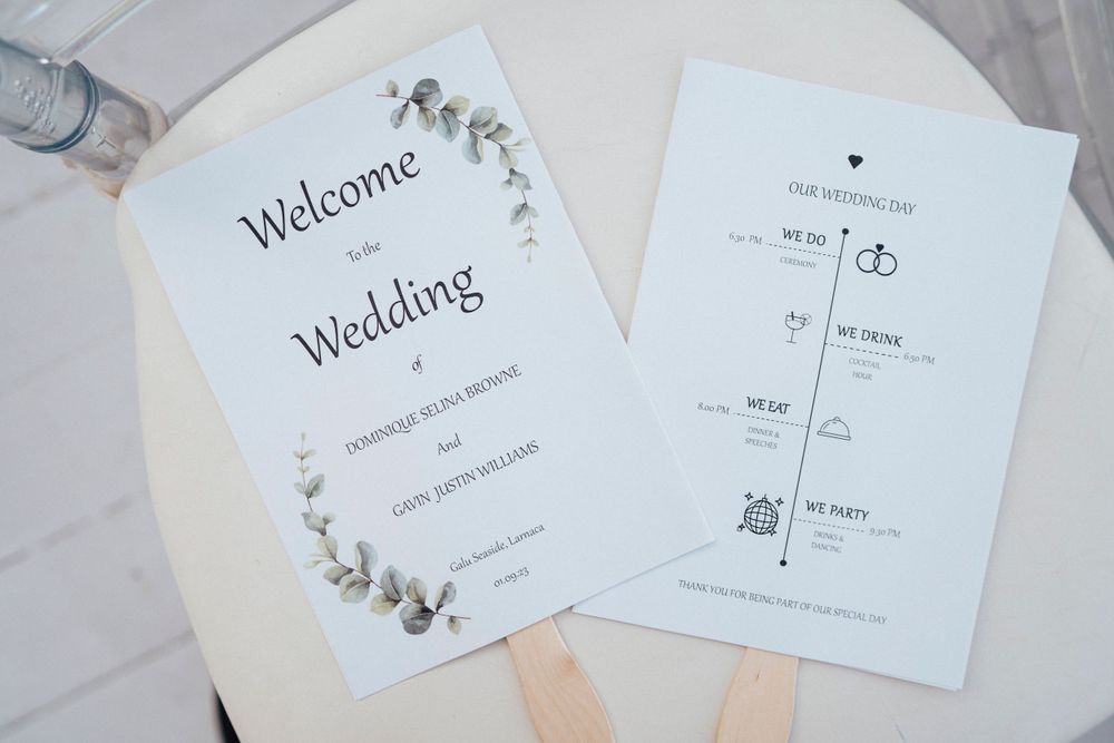 White wedding program fans with floral designs and timeline details lay on a marble surface.