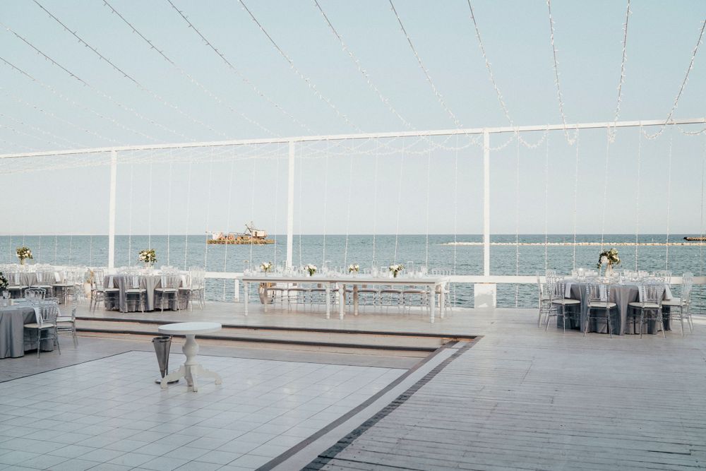 Elegant oceanfront dining terrace with white tables set up overlooking the sea and a wooden deck feature.