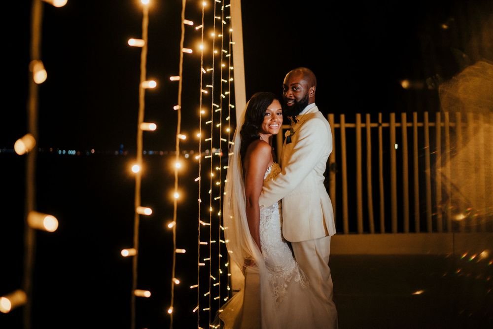 A couple embraces at night with glowing string lights creating a romantic ambiance on their wedding day.
