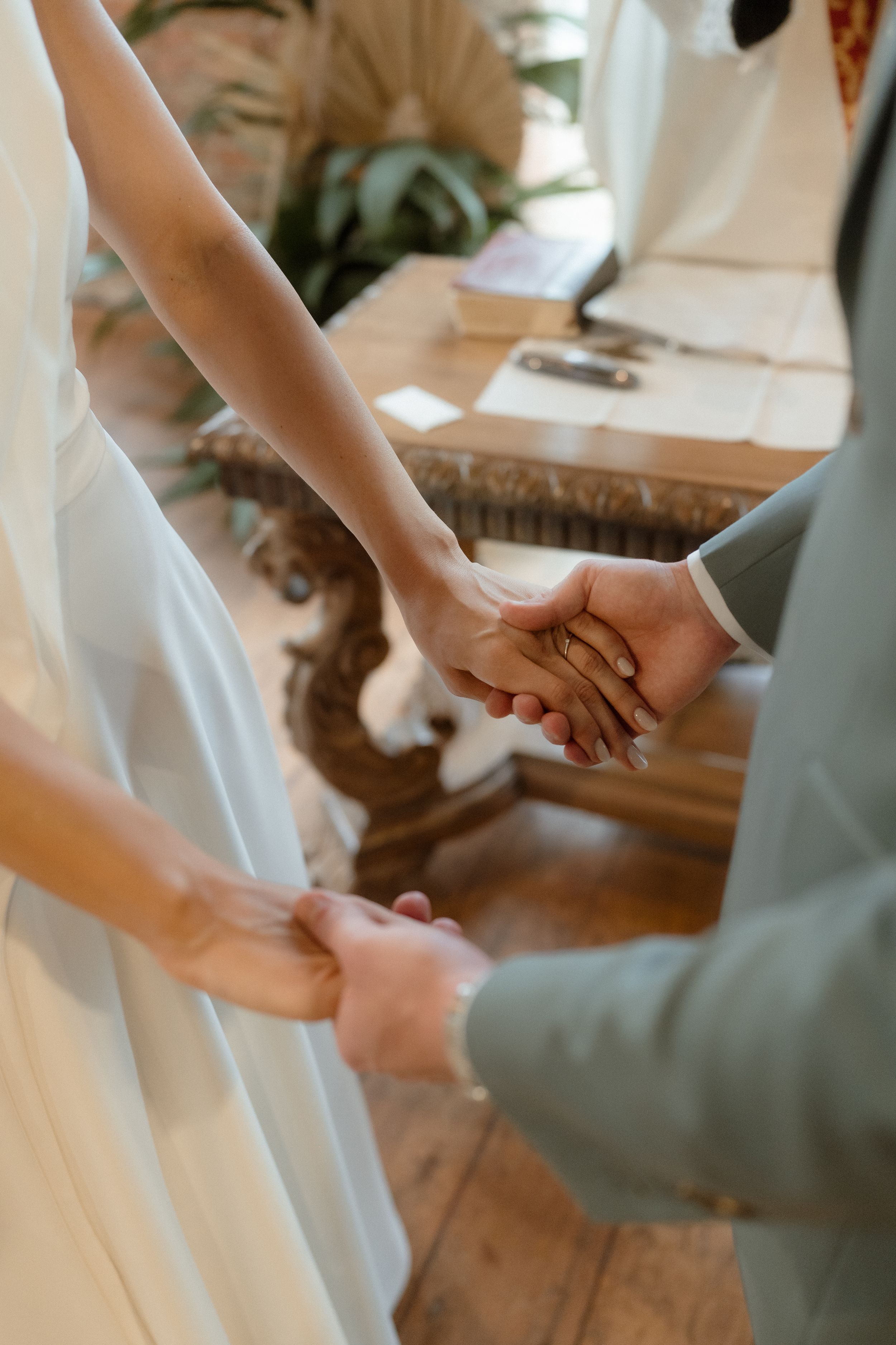 Close-up of couple holding hands during wedding ceremony with white dress detail.