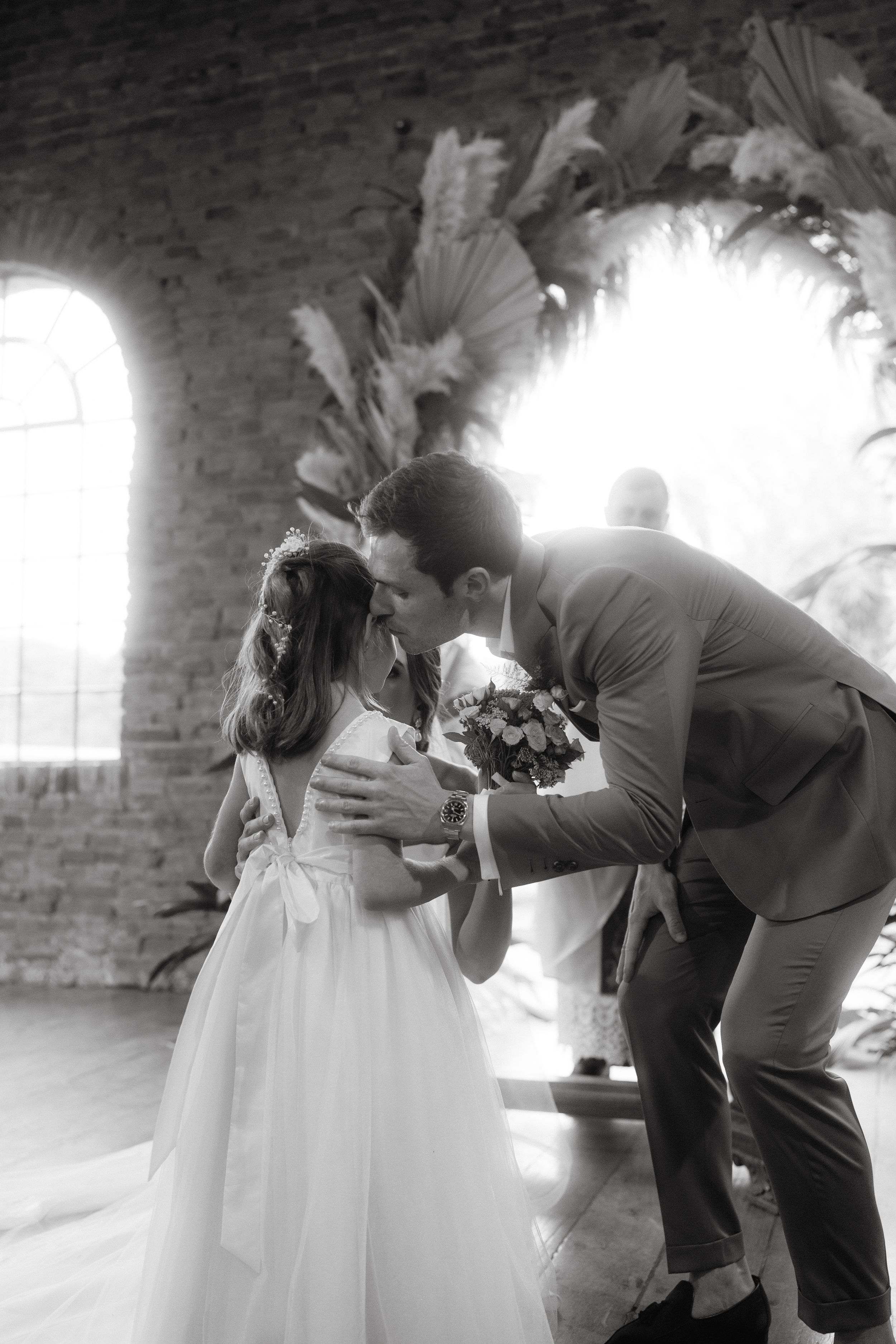 A tender moment between the newlyweds under a beautiful floral arch with natural backlighting in a rustic brick venue.