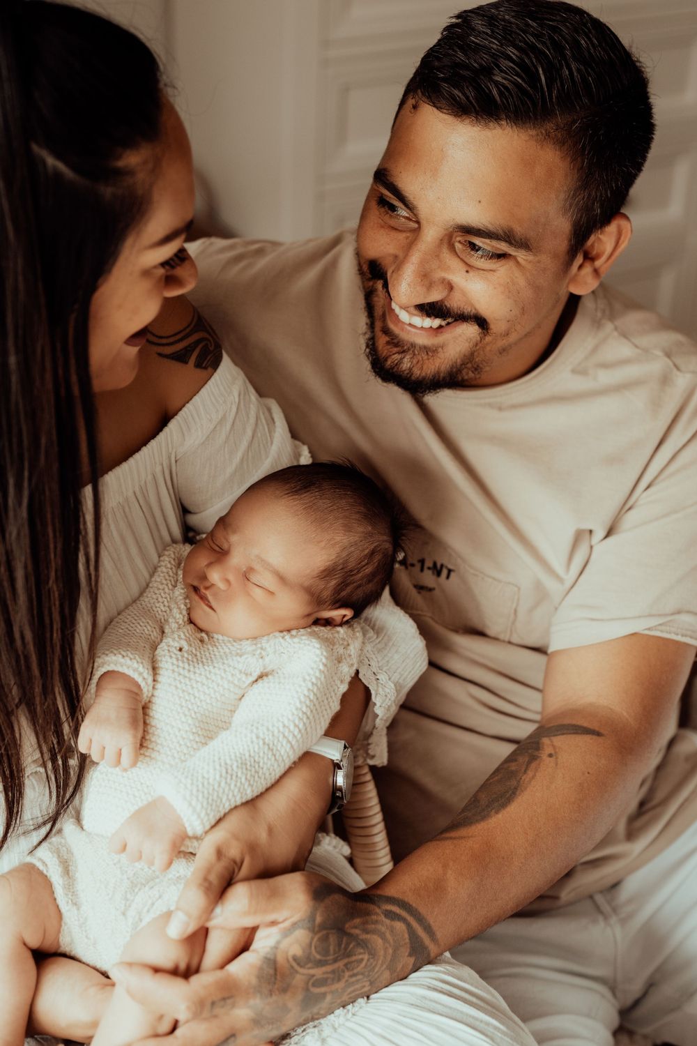 Candid family moment with parents and newborn baby sharing affectionate smiles on white bed.