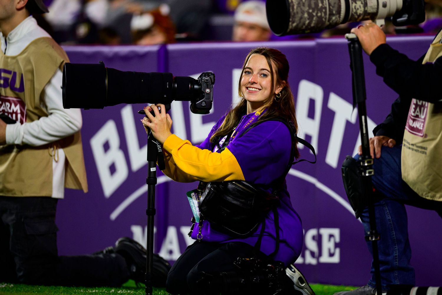 Spirited band member performing in purple and gold uniform at football stadium.