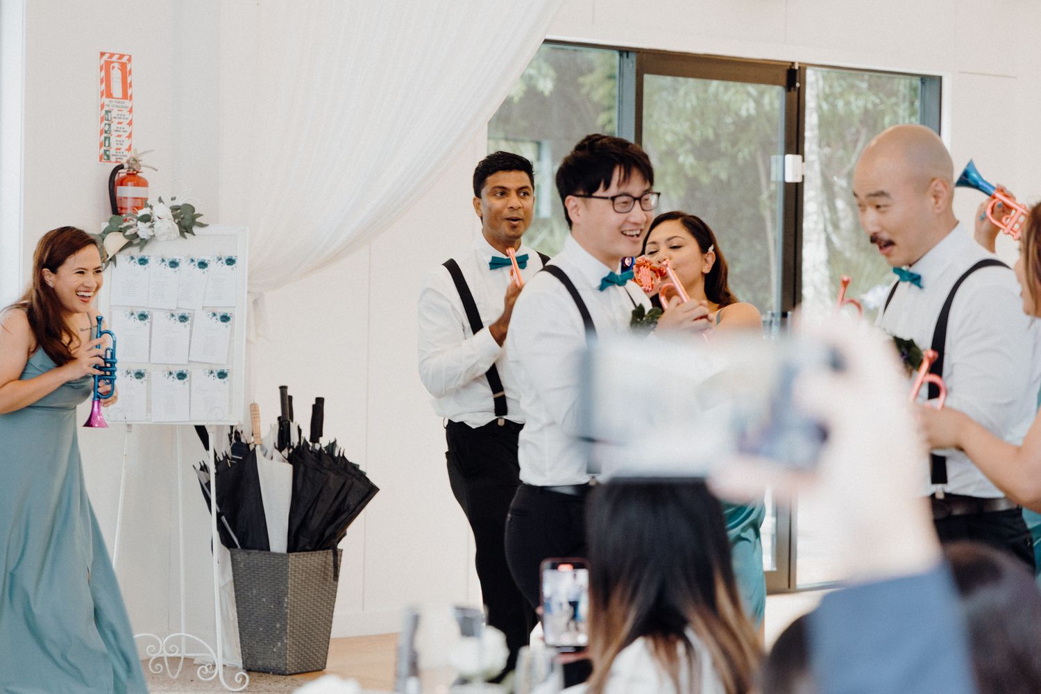Wedding party members dressed in teal and black raise champagne bottles captured by Apertured Media Auckland Wedding Photographer.