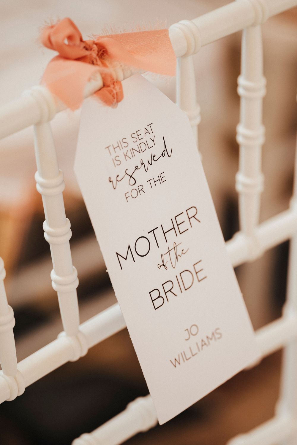 A reserved seat tag for the Mother of the Bride hangs on a white railing with a peach colored ribbon.