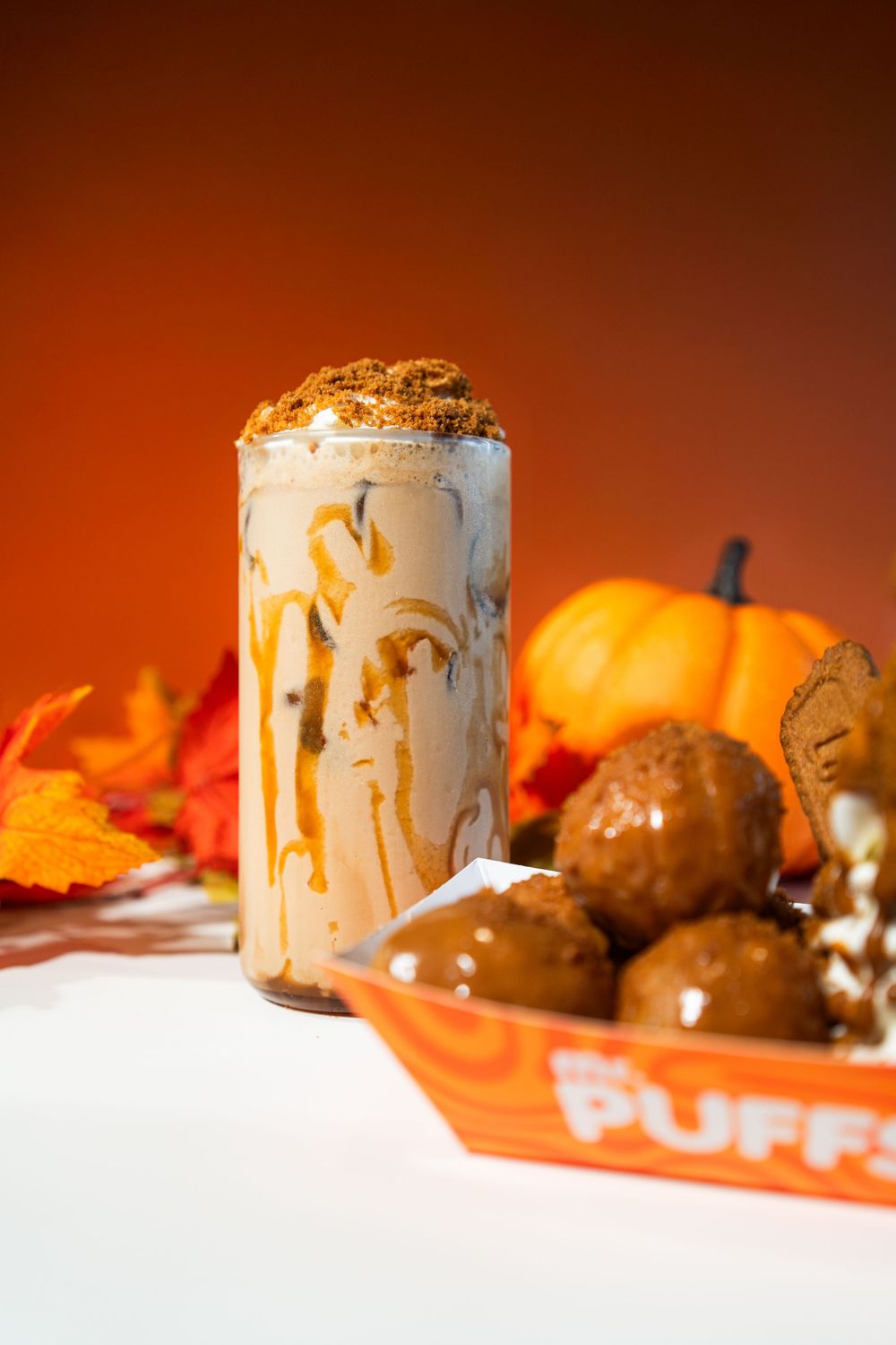 Lit pumpkin spice candles create a warm autumn ambiance with decorative gourds and fall leaves in orange lighting.