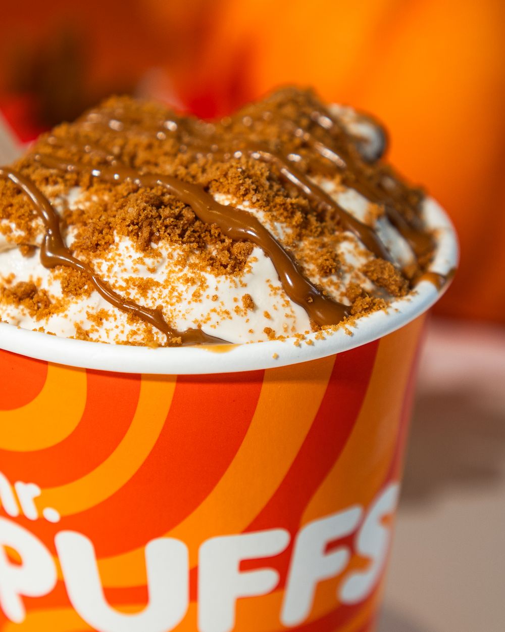 Closeup of whipped cream and crumbled topping on an orange-colored disposable cup in vibrant lighting.