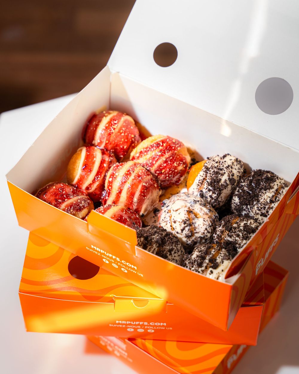Orange branded box filled with colorful desserts including red-drizzled treats and chocolate-covered pastries. Mtlshutter photography