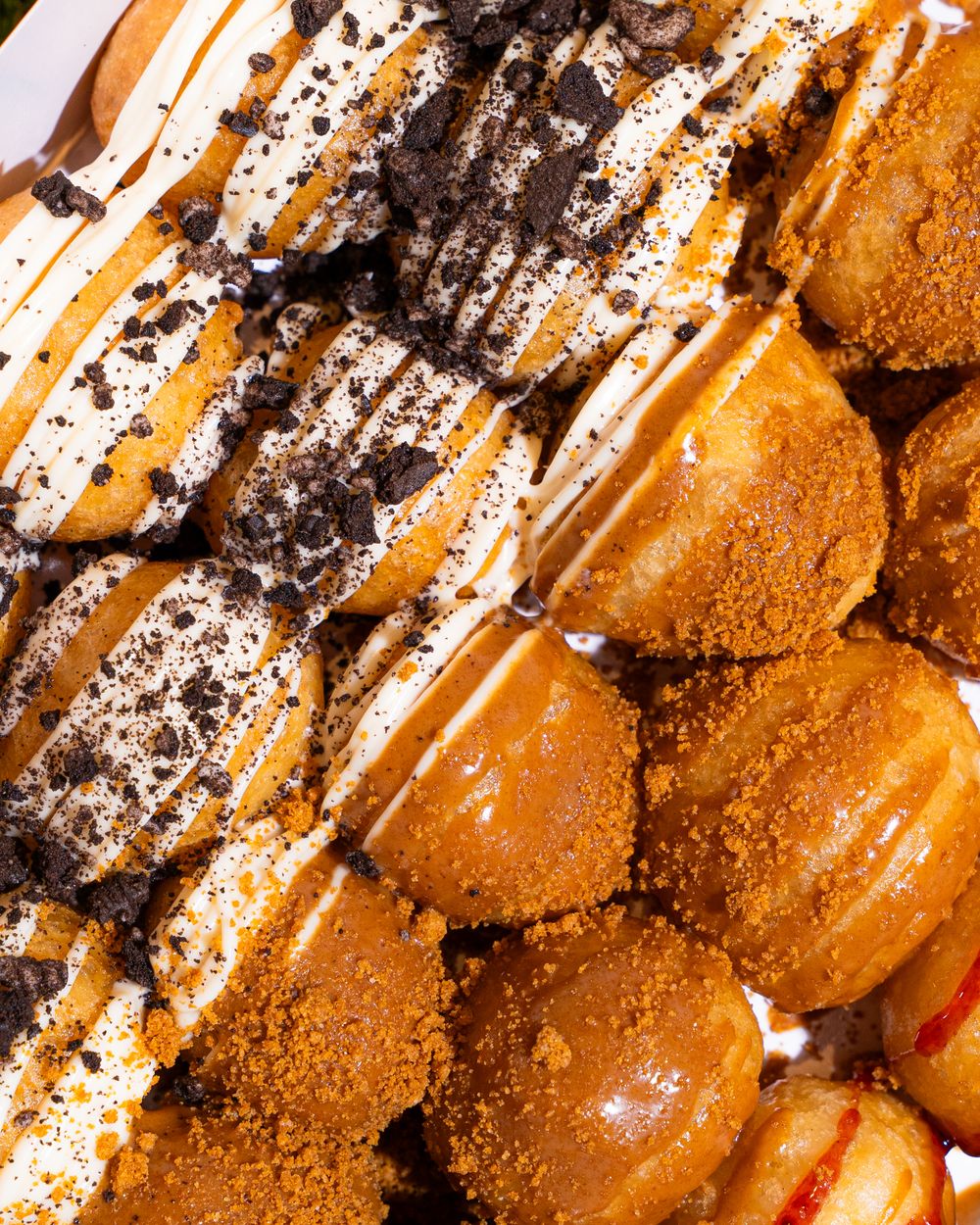 Close-up of assorted gourmet donuts topped with Oreo crumbles, white drizzle, and cinnamon sugar coating.