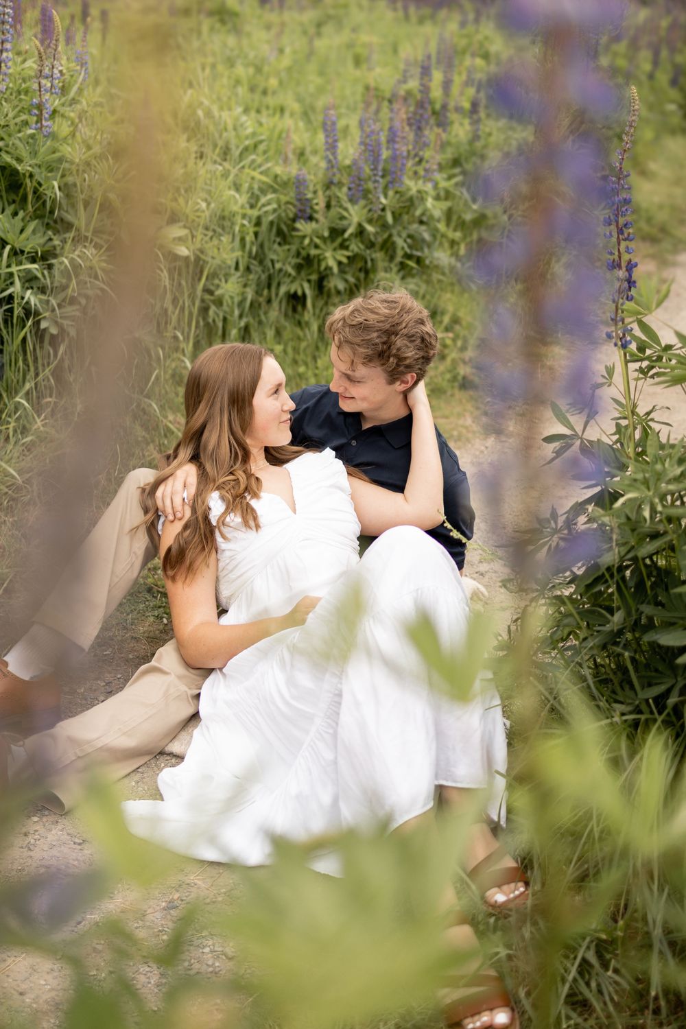 A tender moment between two people sitting among purple wildflowers in soft natural light.