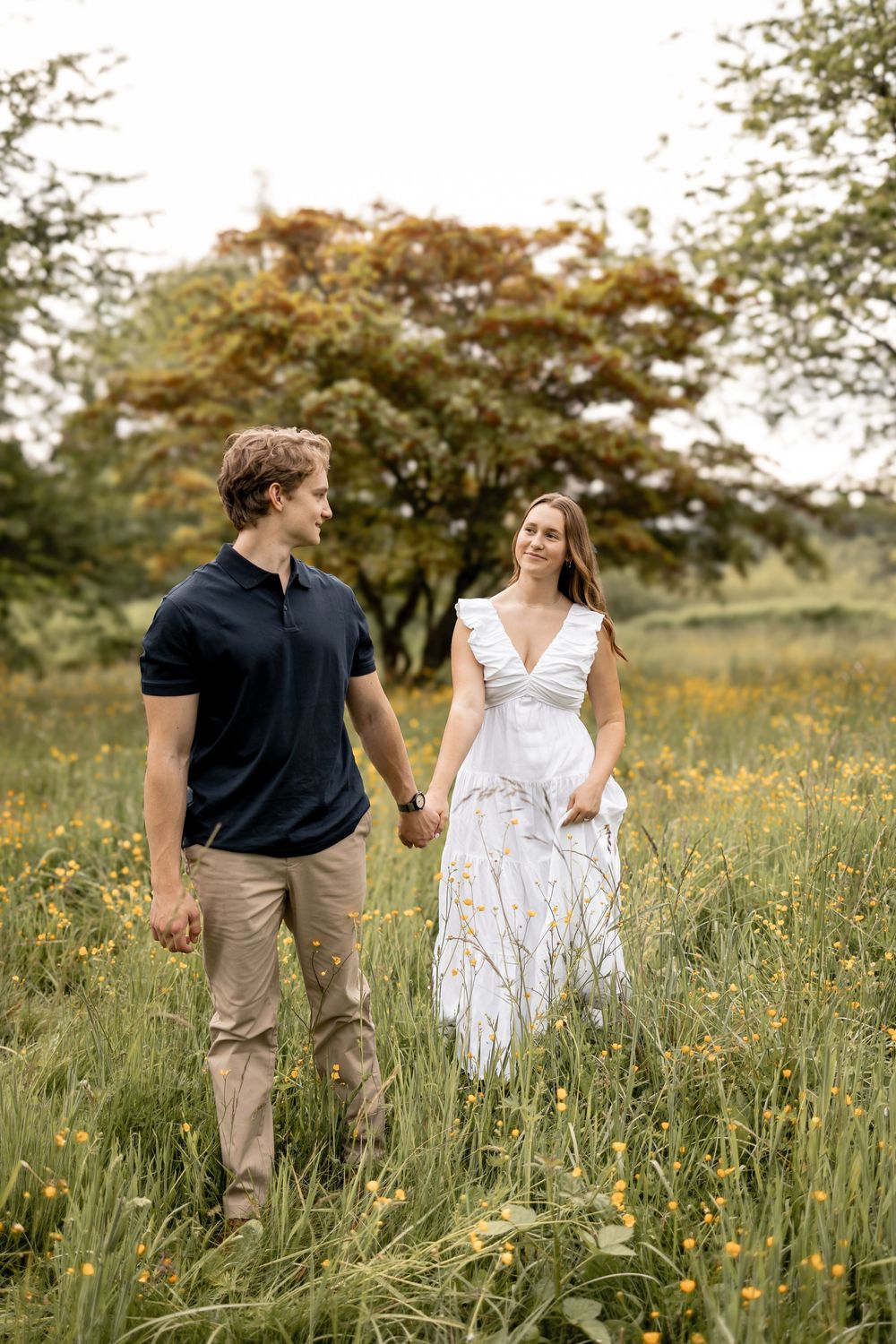 Couple walking through a meadow with wildflowers and tall grass.