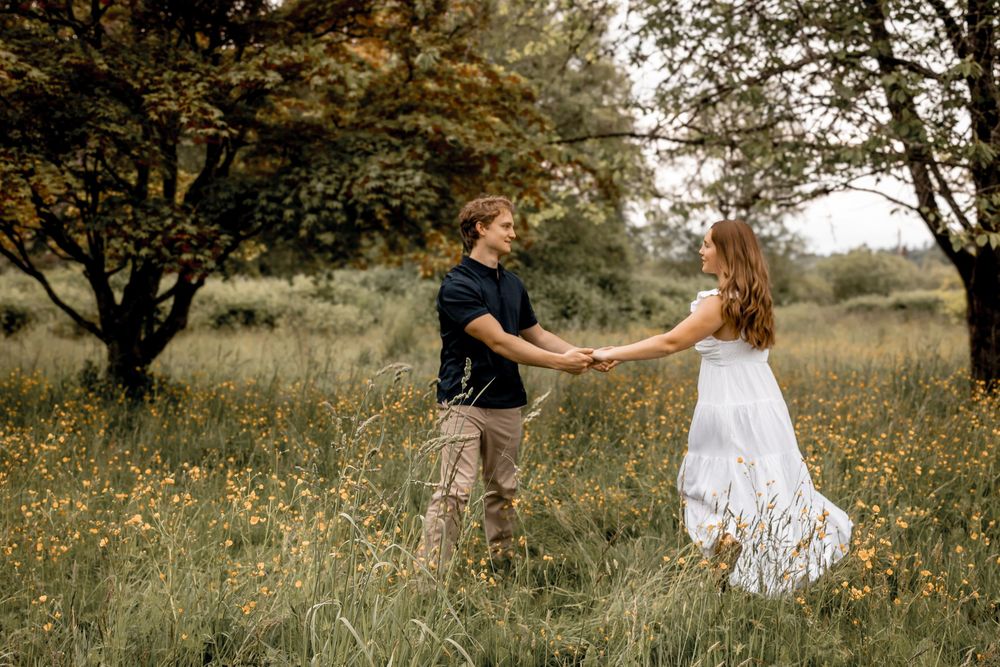 Couple walking and playing in a sunny meadow with scattered wildflowers.