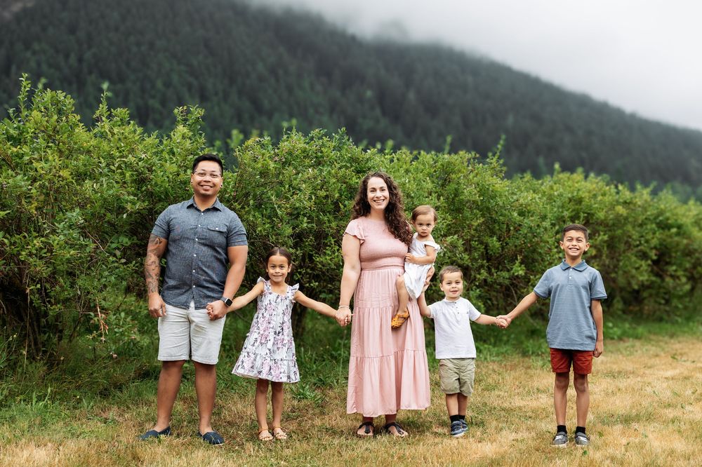 Family standing together in a green field with mountains in background.