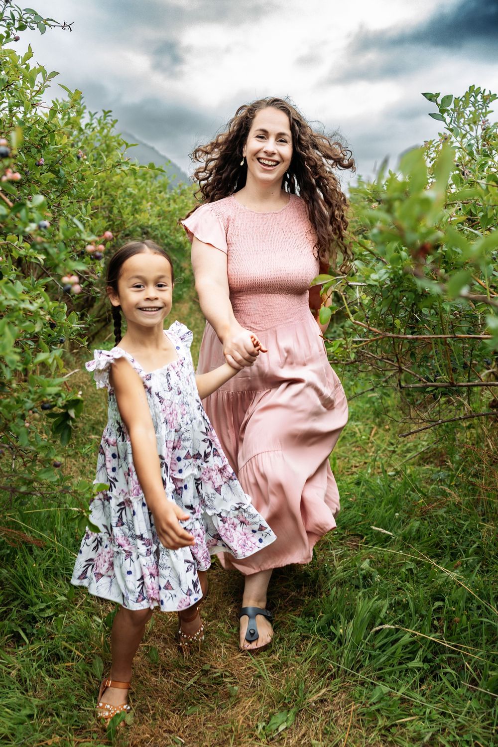 Two people in floral and pink dresses play together in a lush green garden setting.