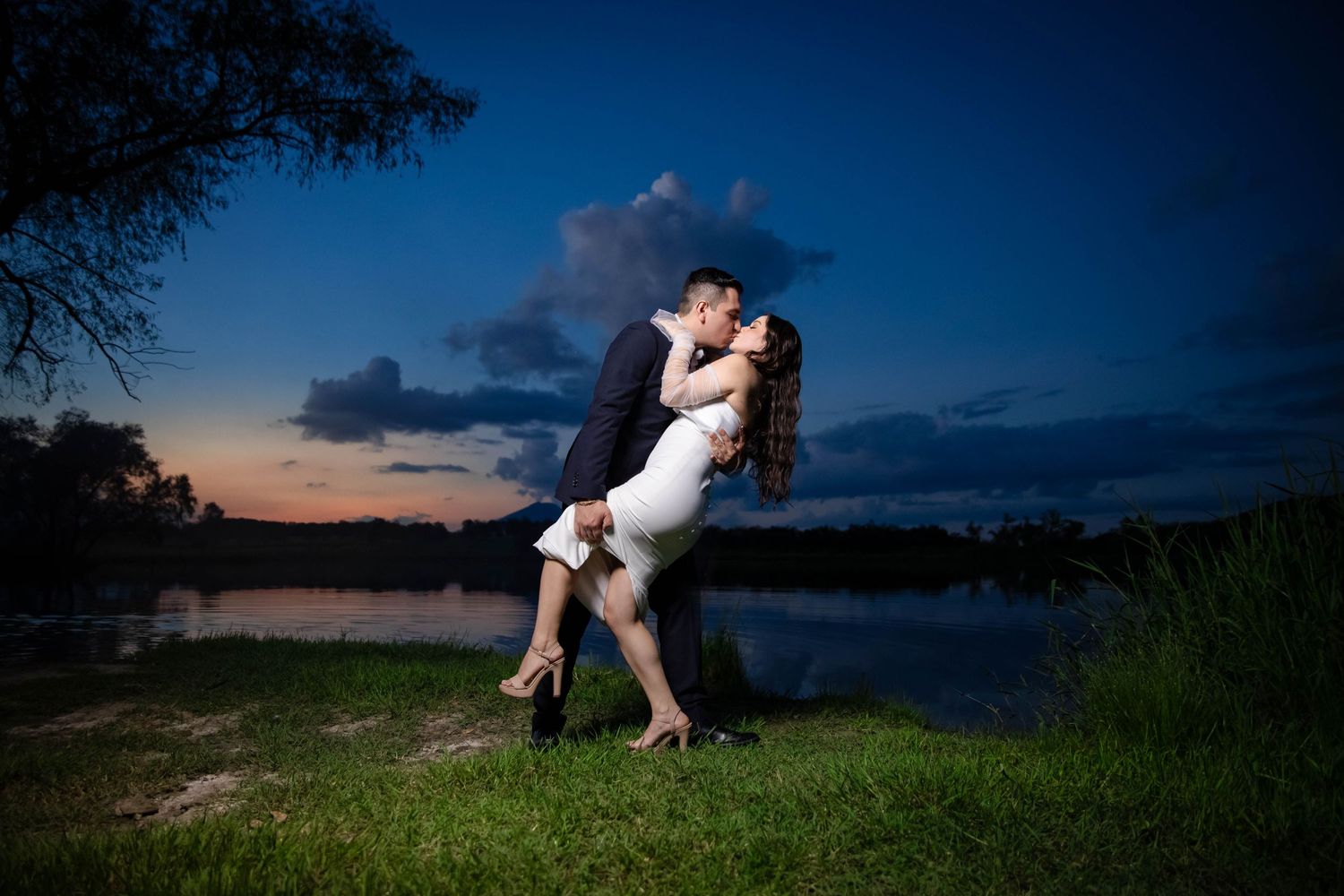 Romantic sunset photo by a lake with dramatic dip pose against blue sky.