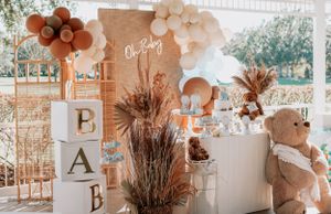 Baby shower display featuring wooden blocks, balloon arch, and dried pampas grass in peach and cream colors.