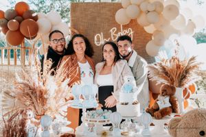 Baby shower celebration with guests posing at decorated dessert table with balloon arch.