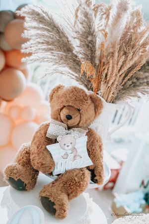 Brown teddy bear with blue bow tie decorations and pampas grass arrangements.