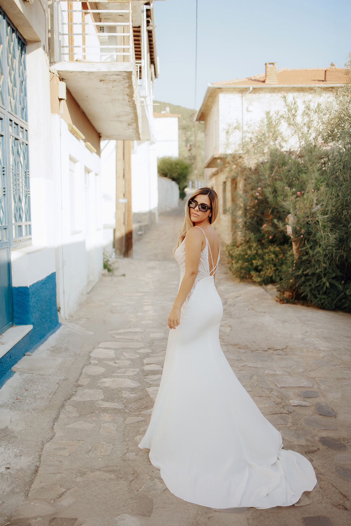 Elegant white wedding dress with fitted silhouette and flowing train on a charming Mediterranean-style street.