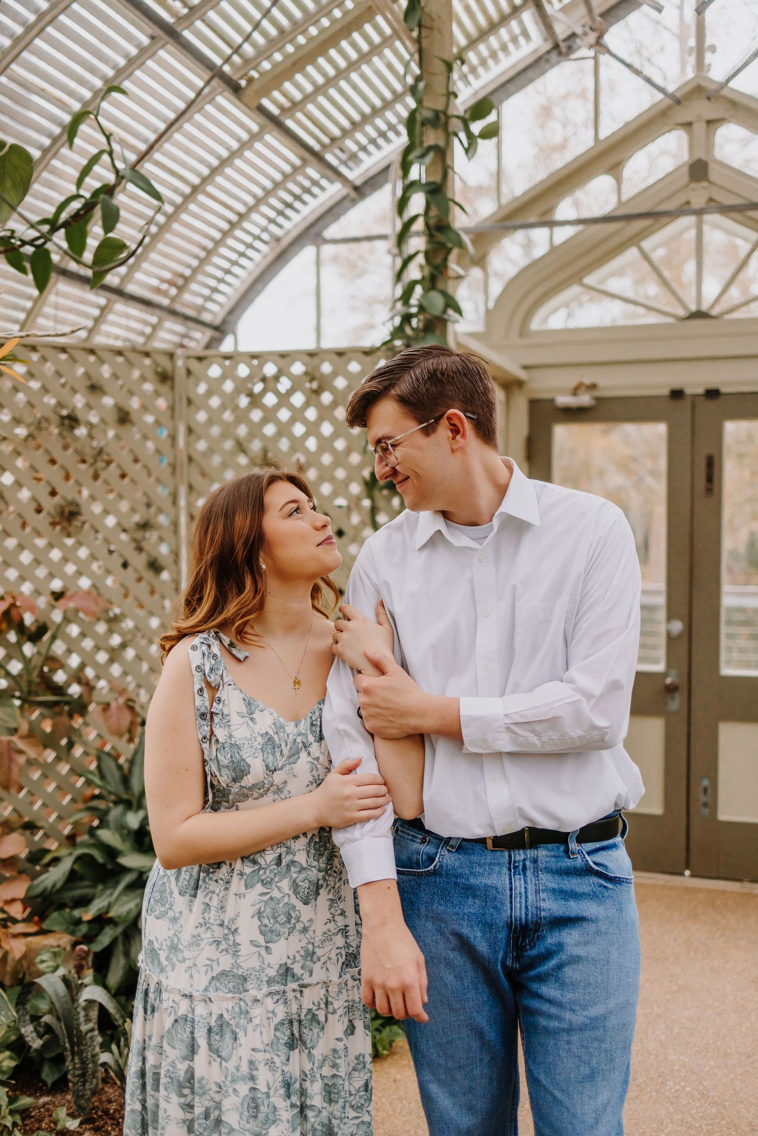 Romantic couple shares intimate moments in a sunlit greenhouse with latticed windows and climbing plants.