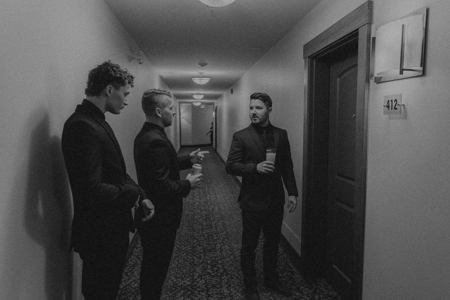 Three people having a conversation in a dimly lit hotel hallway captured in black and white.