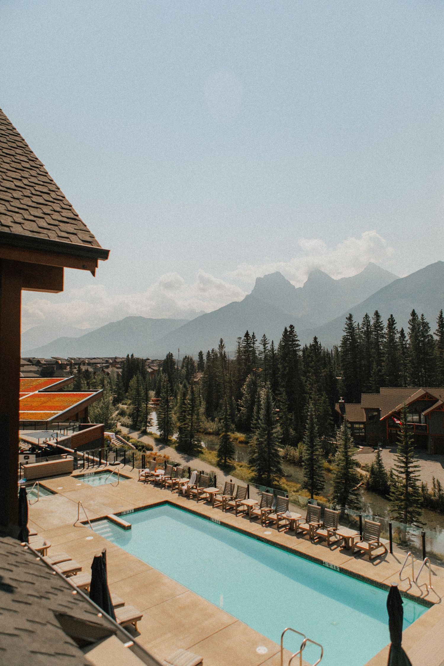 Mountain resort pool with lounge chairs overlooking scenic forest and mountain peaks.